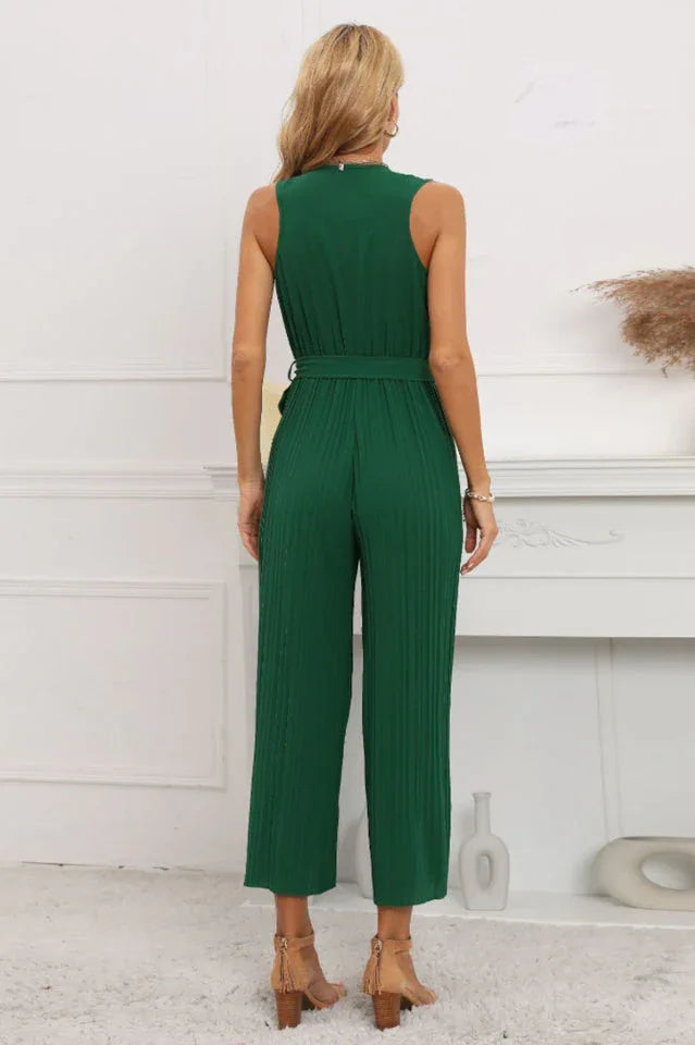 Back view of a woman in a green sleeveless pleated jumpsuit with a tie belt.