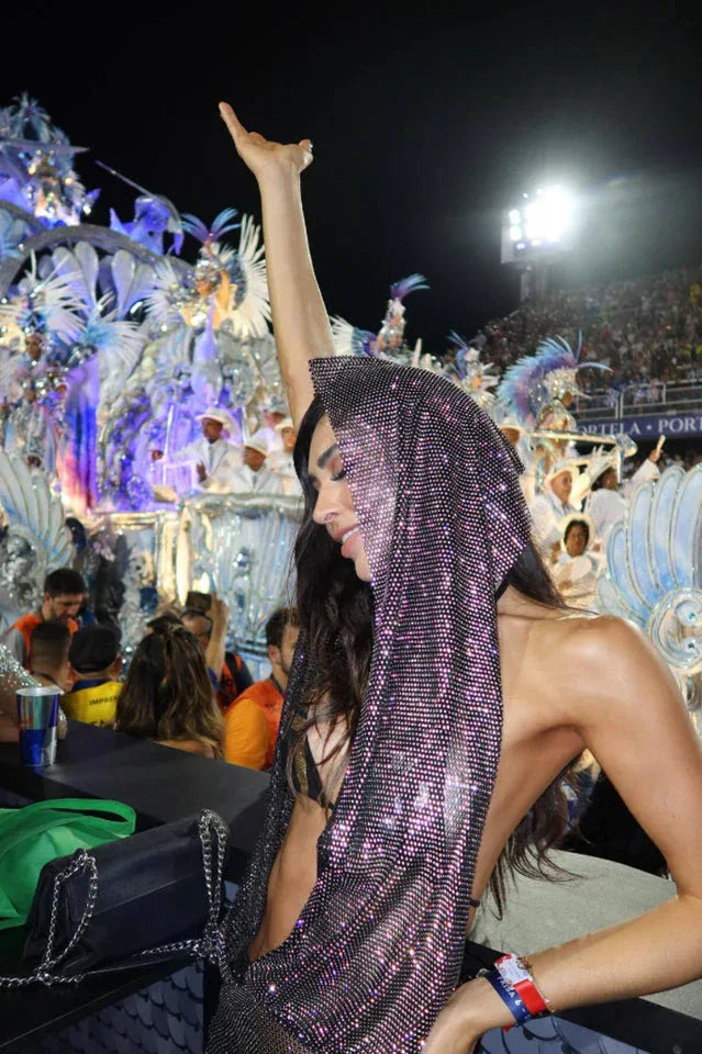 Woman with her arm raised, wearing a hooded sparkling mesh top at a lively celebration.
