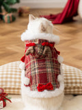 Rear view of a white cat in a red plaid Christmas cape with faux fur trim and decorative bows.