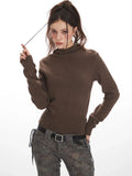 Woman wearing a brown turtleneck sweater and patterned pants, holding her hair
