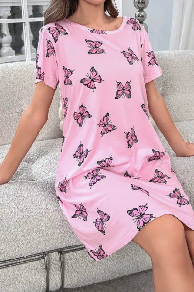 Woman sitting on a couch wearing a pink short-sleeve nightgown with a scattered pink butterfly print.