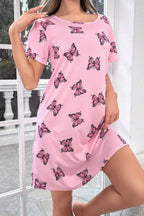 Woman posing in a pink short-sleeve nightgown with a scattered pink butterfly print, with a window in the background.