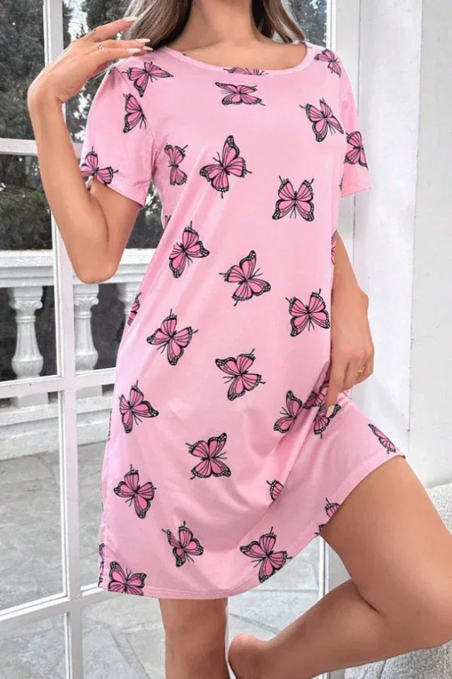 Woman posing in a pink short-sleeve nightgown with a scattered pink butterfly print, with a window in the background.
