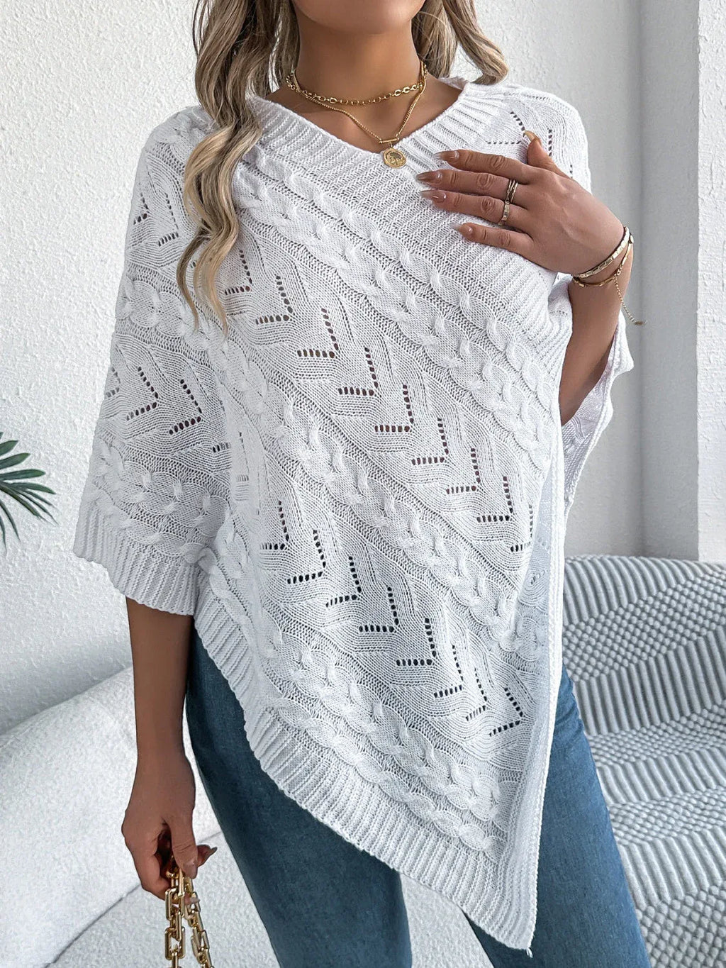 Close-up of a woman's chest and shoulder wearing a white V-neck knit poncho.