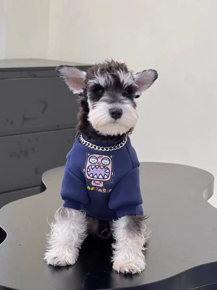 Miniature schnauzer puppy wearing a navy blue dog sweatshirt with a pink monster graphic on the front and a silver chain collar.