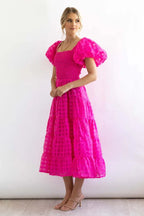 Side profile of a woman showcasing the puff sleeves and tiered design of a pink checkered dress.