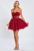 Model presenting a short, strapless red party dress with intricate rose detailing on the skirt and a beaded bodice, held with a small white clutch.