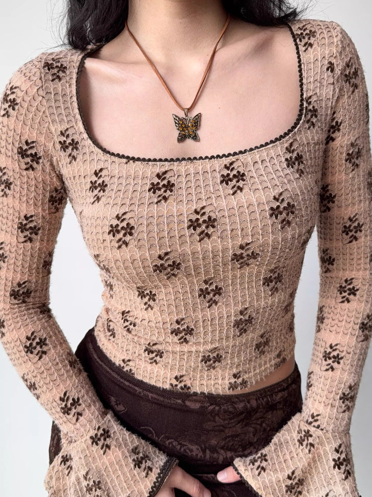 Close-up of a woman wearing a beige long-sleeved top with a brown floral print and a square neckline.