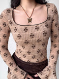 Close-up of a woman wearing a beige long-sleeved top with a brown floral print and a square neckline.