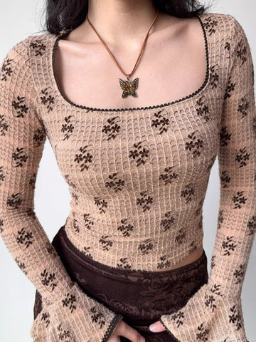 Close-up of a woman wearing a beige long-sleeved top with a brown floral print and a square neckline.