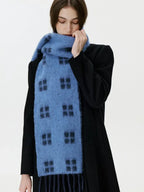 Woman with her hand near her face wearing a blue scarf with a black windowpane plaid pattern