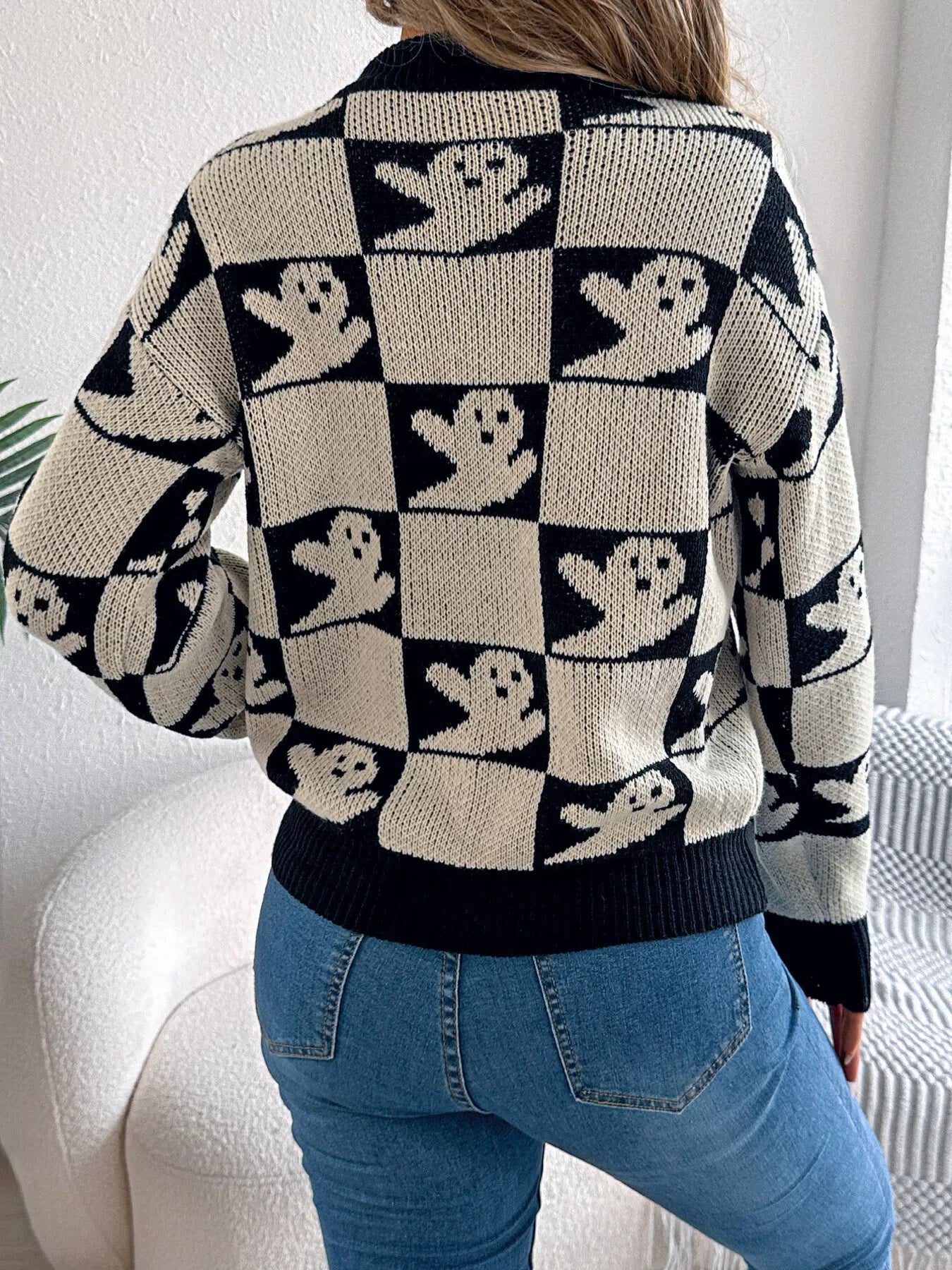 Back view of a woman wearing a black and cream checkerboard knit sweater with ghost print and blue jeans.