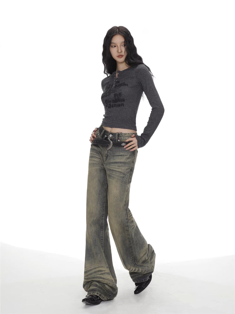 Full body shot of a woman in a grey long-sleeve graphic print cropped top and wide-leg jeans.