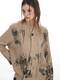Detailed view of the neckline and button closure on a tan knit cardigan with abstract black print.