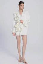 A woman models a white blazer adorned with fabric flowers, presented against a plain background.