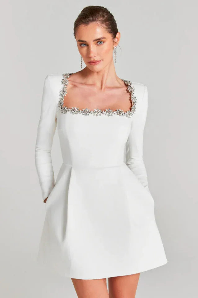 Woman wearing a white long-sleeved A-line dress with a square neckline adorned with crystals