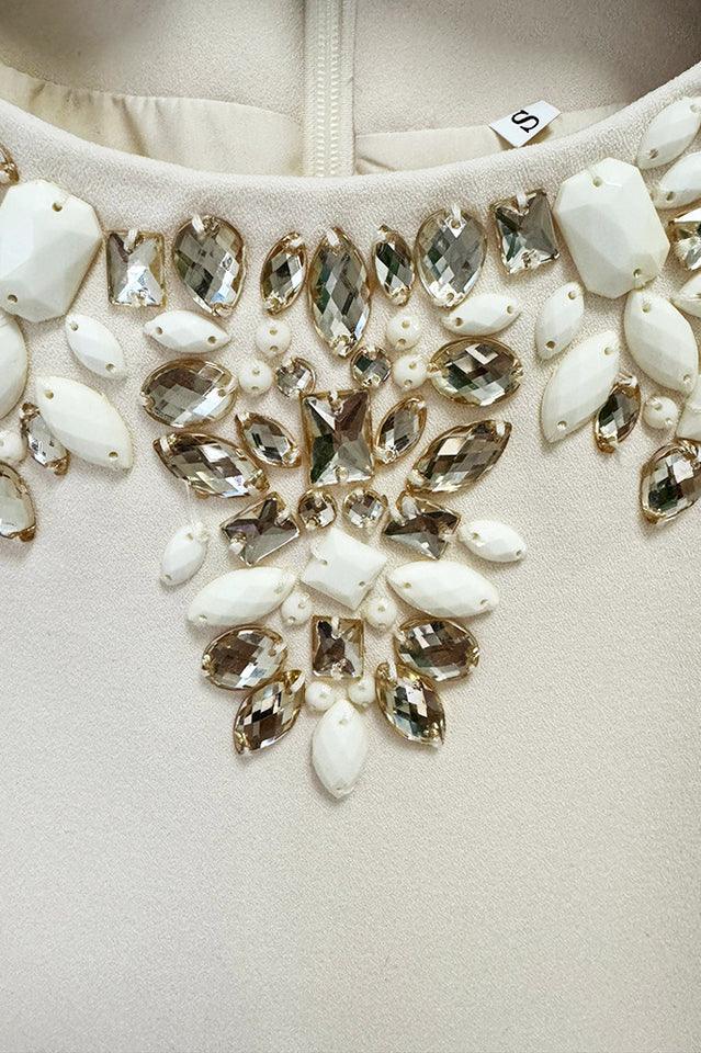 Detailed view of the embellished neckline of a cream mini dress, featuring a mix of clear and opaque crystals.