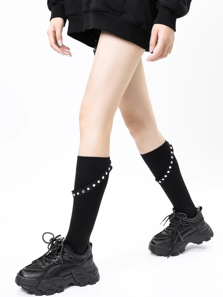 Black knee-high socks with decorative silver studs and adjustable straps, worn with chunky sneakers.