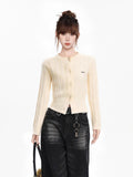 Full body shot of a woman in a cream cable knit cropped cardigan, dark wash wide-leg jeans, and accessories.