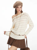 Close-up of a model wearing a cream-colored off-the-shoulder knit sweater with a diamond pattern and decorative trim. The sweater is styled with a decorative belt and a brown textured mini skirt.