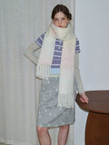 Woman wearing a long, thick scarf with an ombre gradient of pastel pink and cream, draped around her neck over a striped shirt and star-print skirt.