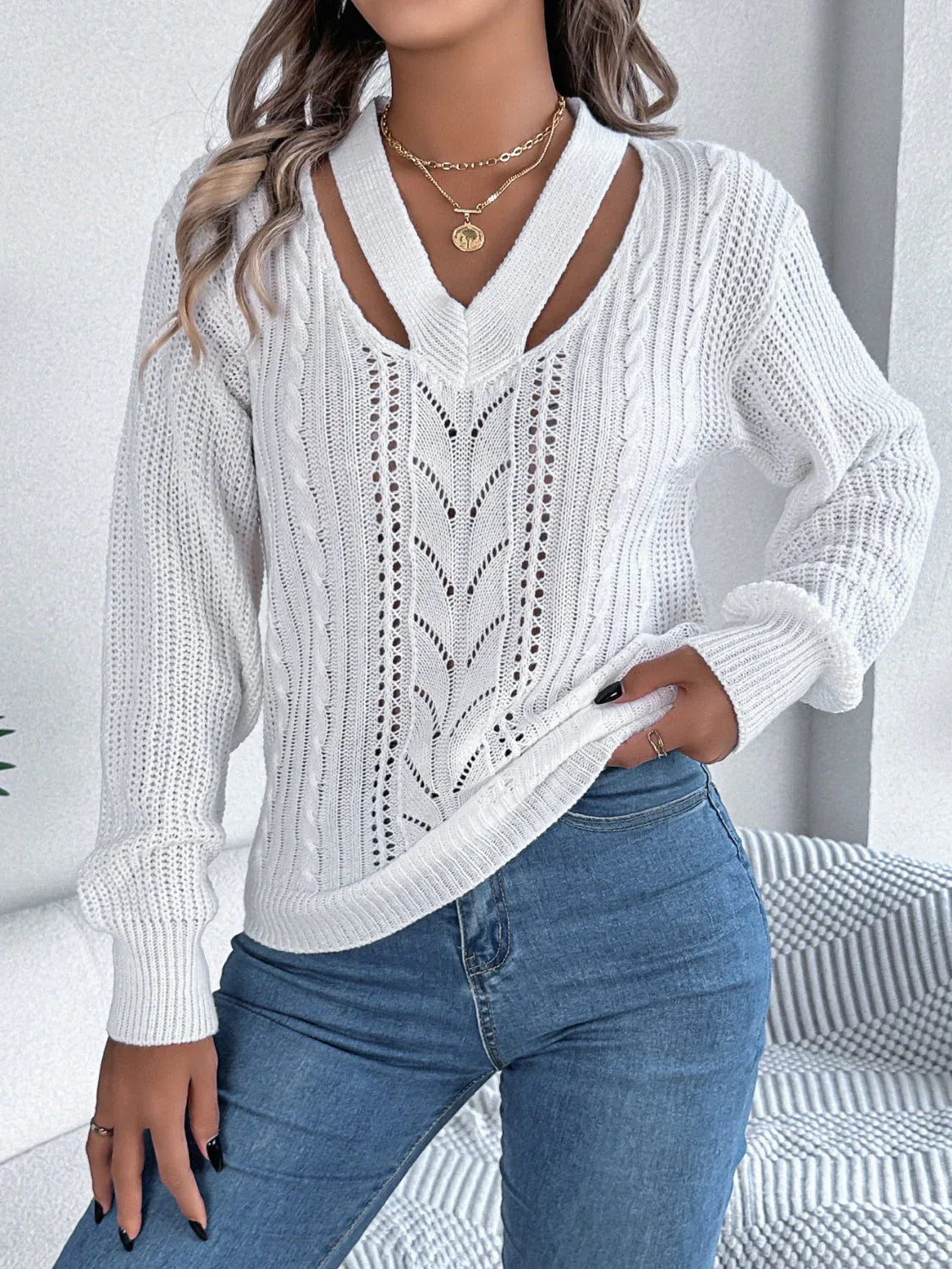 Woman wearing a white long-sleeve knit sweater with a cut-out V-neck and cable knit details. Main image