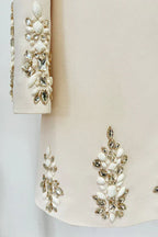 Detail of the embellished cuffs and hem of a cream long-sleeve mini dress with sparkling crystal and pearl accents.