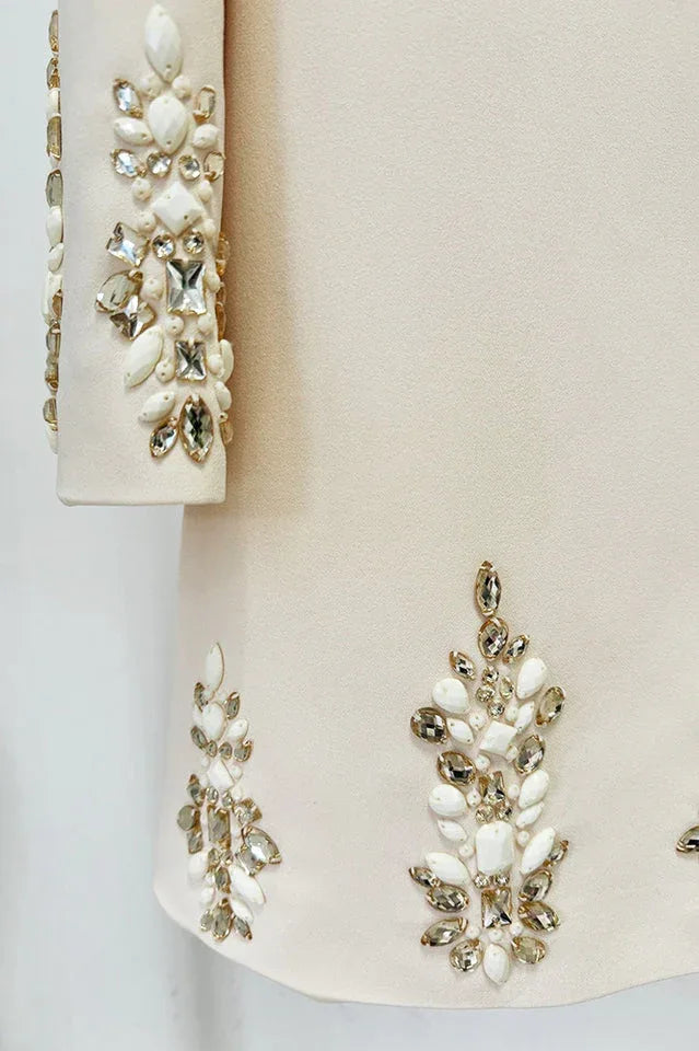 Detail of the embellished cuffs and hem of a cream long-sleeve mini dress with sparkling crystal and pearl accents.