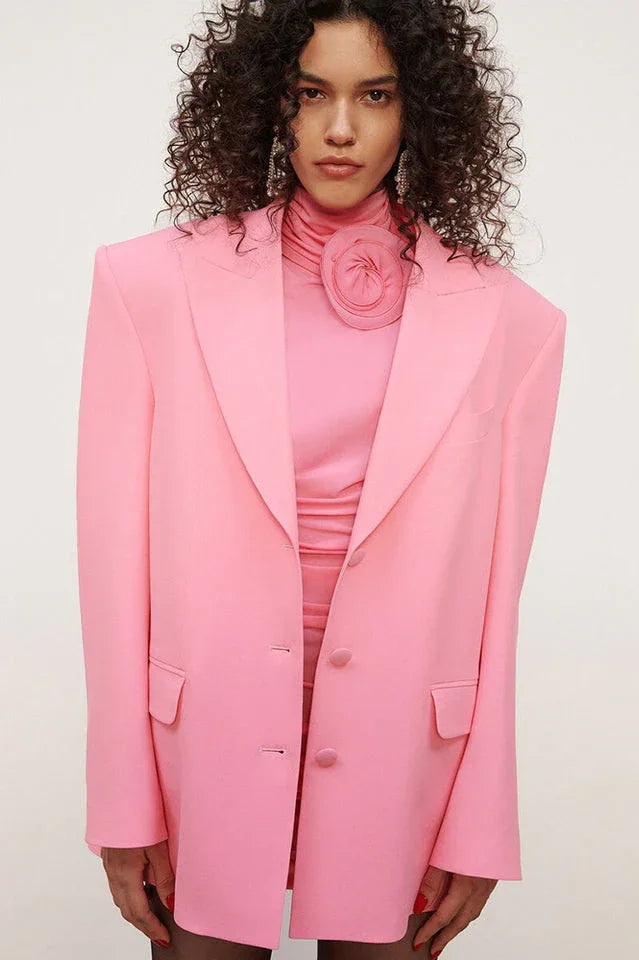 Close-up of a pink ruched dress with a flower detail at the neckline, worn with a pink blazer.