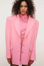 Close-up of a pink ruched dress with a flower detail at the neckline, worn with a pink blazer.