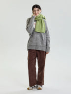 Full body shot of a woman wearing a light green ribbed knit scarf and a grey sweater.