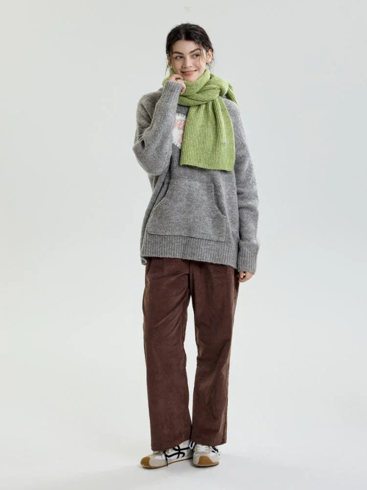 Full body shot of a woman wearing a light green ribbed knit scarf and a grey sweater.