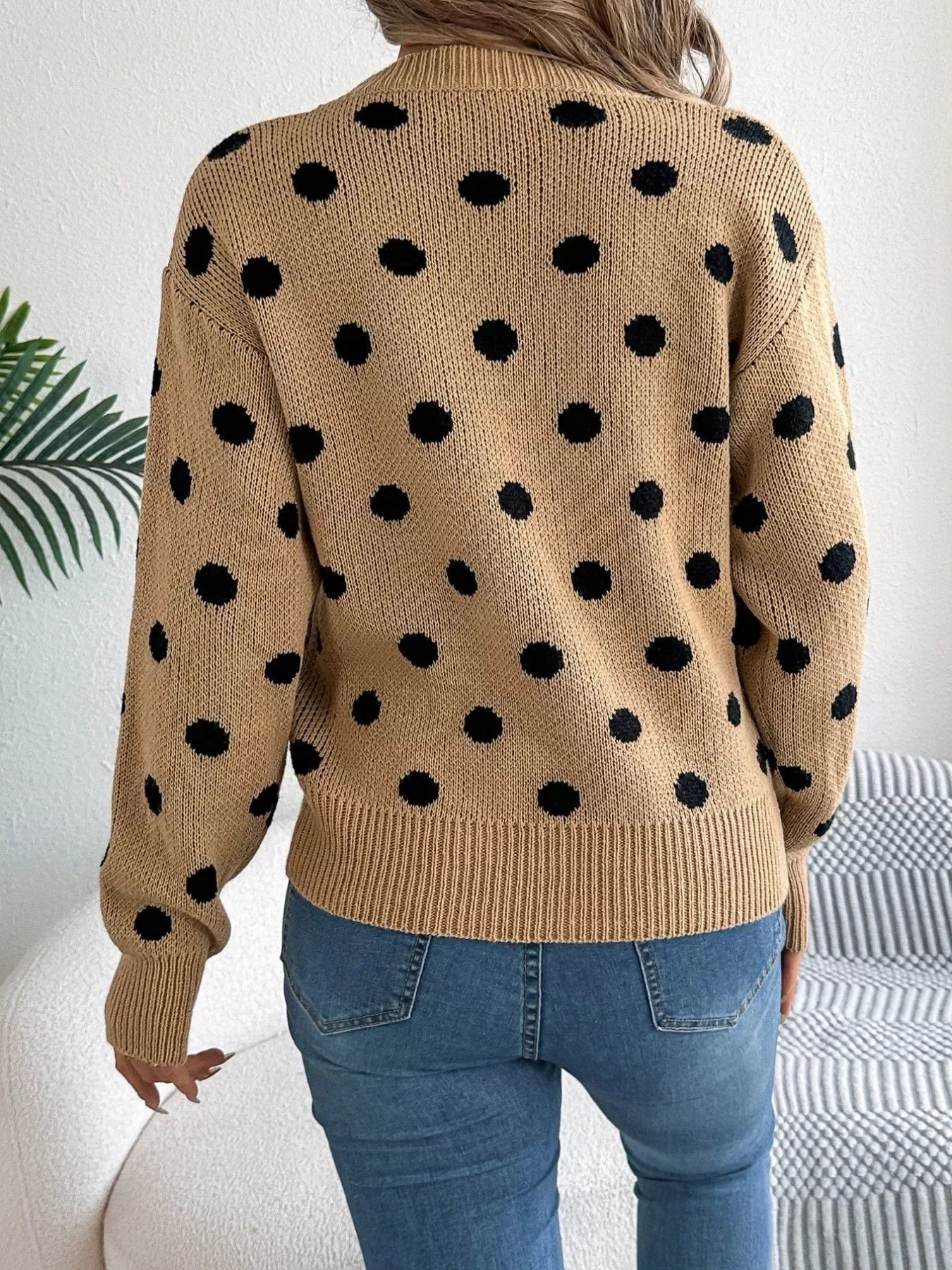 Back view of a woman in a tan polka dot sweater and blue jeans.