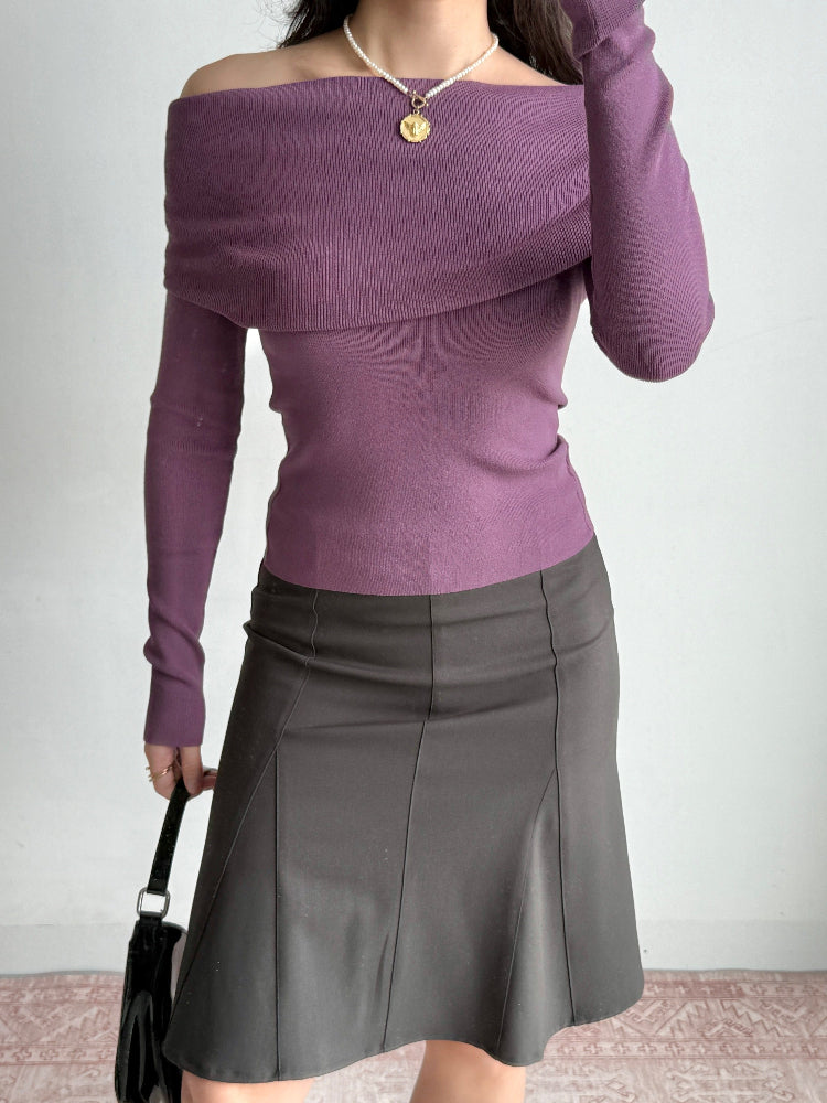 Woman in a purple off-the-shoulder top, dark skirt, and holding a black handbag.