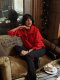 Woman in a red textured knit half-zip sweater and black pants sitting on a couch.
