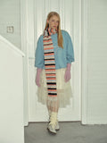 Woman wearing a light blue sweatshirt, a white tulle skirt, pink gloves, white socks, and sneakers, with a multi-colored striped scarf around her neck.
