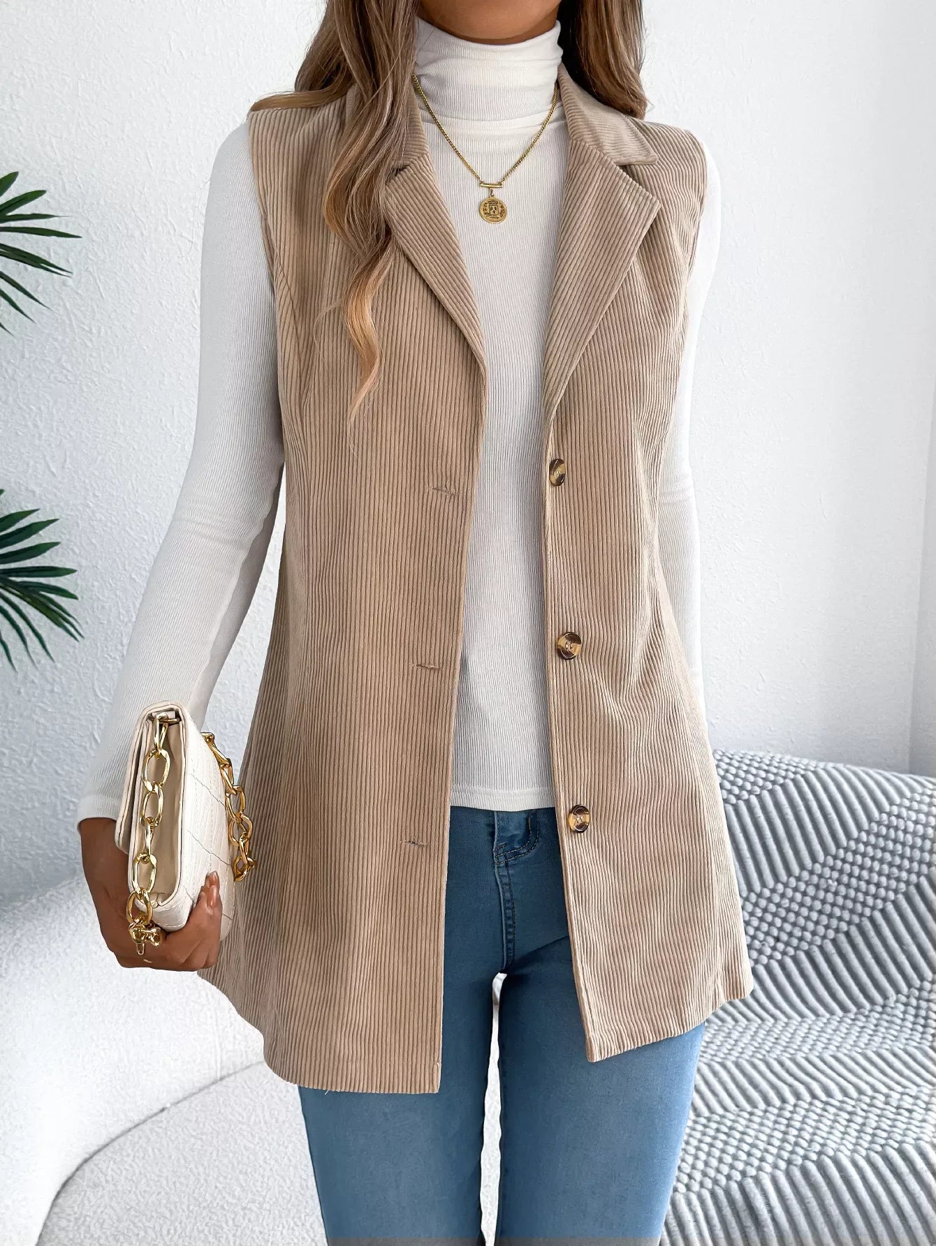 Woman wearing a beige corduroy longline vest over a white turtleneck and blue jeans.