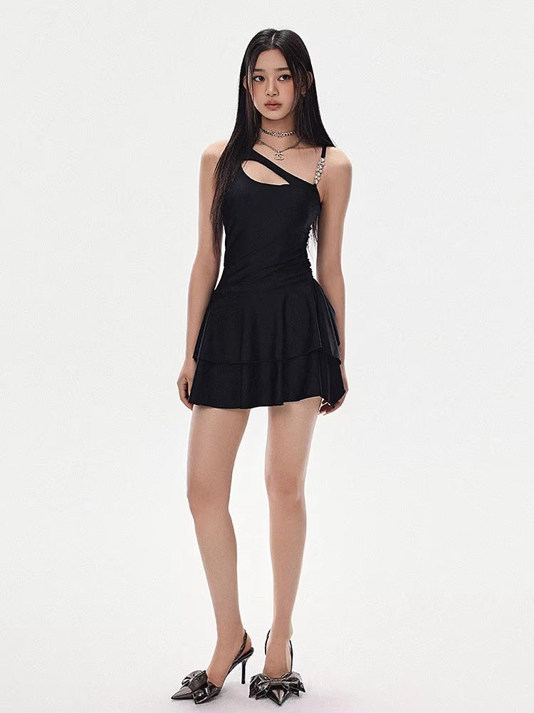 Woman in a black one-shoulder dress with a tiered skirt and high heels, standing and looking forward