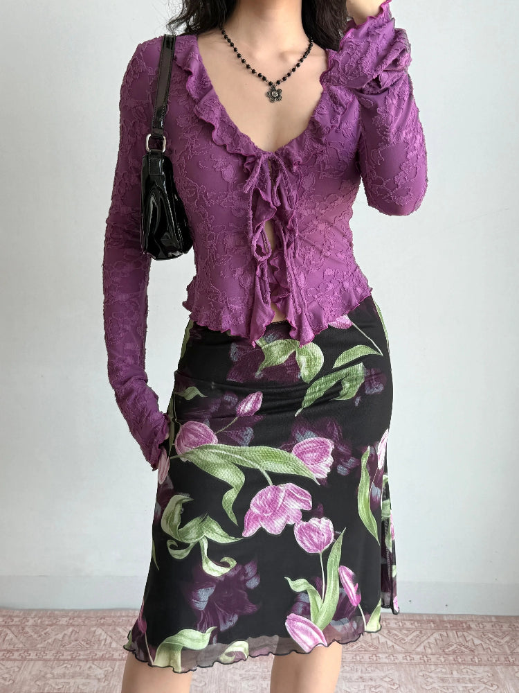 Full body shot of a woman wearing a purple textured mesh long-sleeve top paired with a floral print skirt.