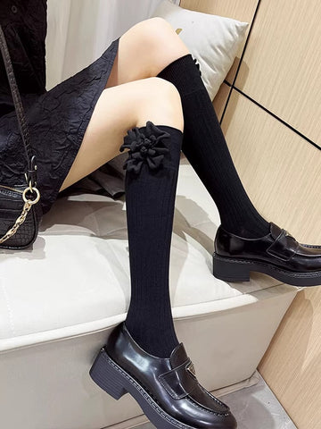 black knee-high socks with ribbed texture and a black flower applique on the cuff