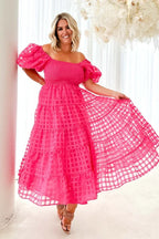 Woman posing in a bright pink tiered midi dress with voluminous puff sleeves and a smocked bust.