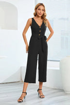 Woman wearing a black sleeveless V-neck culotte jumpsuit with a tie waist and button details
