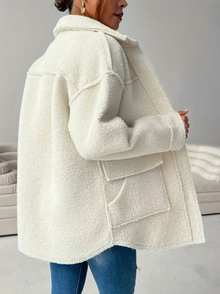 Back view of a woman in a cream-colored oversized fleece jacket, showcasing the textured fabric and hip pockets.