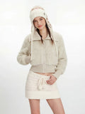 Woman posing in a cream fuzzy cropped jacket and white knit mini skirt