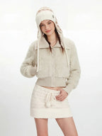 Woman posing in a cream fuzzy cropped jacket and white knit mini skirt