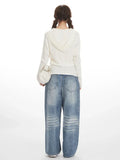 Rear view of a woman wearing a white ribbed knit long-sleeve top with a detachable hood, paired with light-wash baggy jeans.
