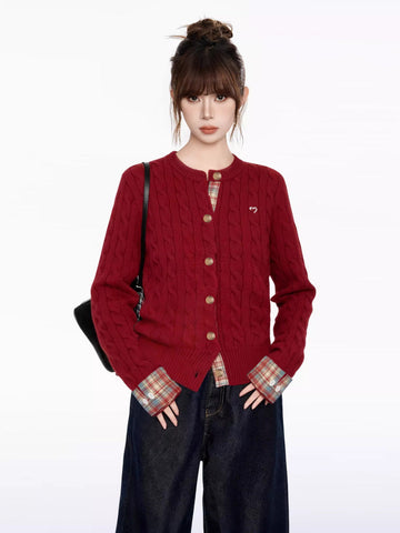 Woman wearing a red cable knit cardigan with a crew neckline and long sleeves, featuring embroidered heart detail and contrast plaid cuffs.