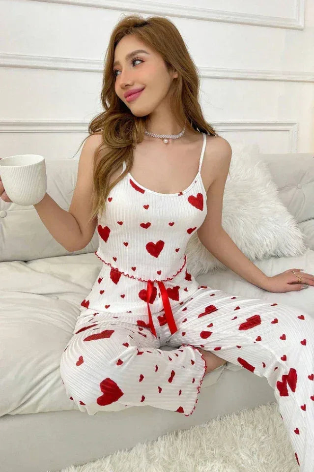 Woman in heart print sleepwear set sitting on a sofa, holding a cup and saucer.