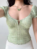 Front view of a woman wearing a green floral print ribbed knit top with a tie front and puff sleeves.