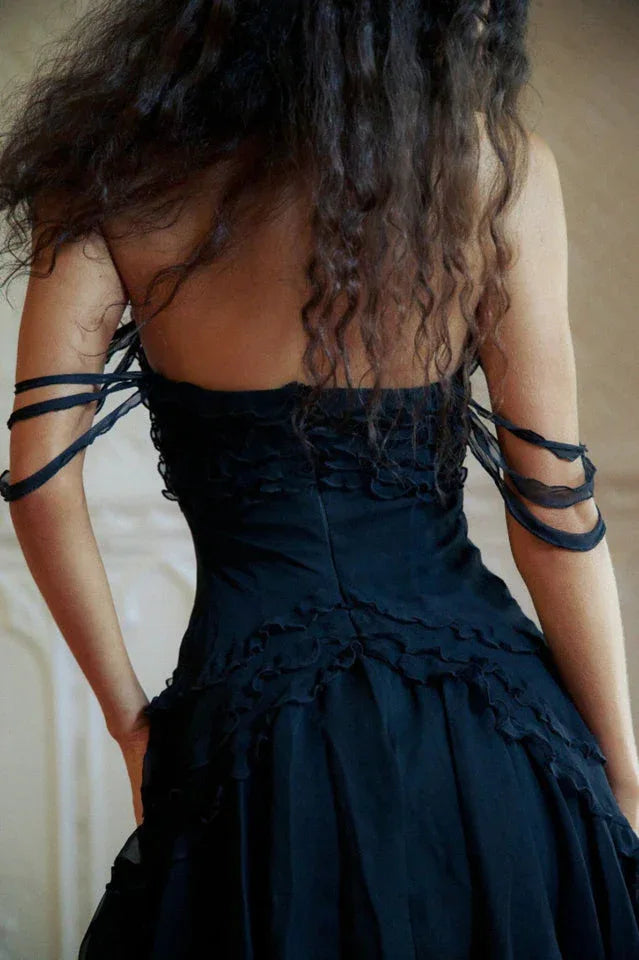 Close-up back view of a woman's shoulders and upper back in a black dress with ribbon straps